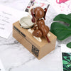 A robotic dog piggy bank made of brown and white materials sits next to some paper and a green leaf.