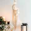 Boho macrame dream catcher wall decor featuring a crescent moon and hanging fringe on a white wall.