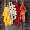Dried corn and various colorful fruits and vegetables hanging on a wooden rack