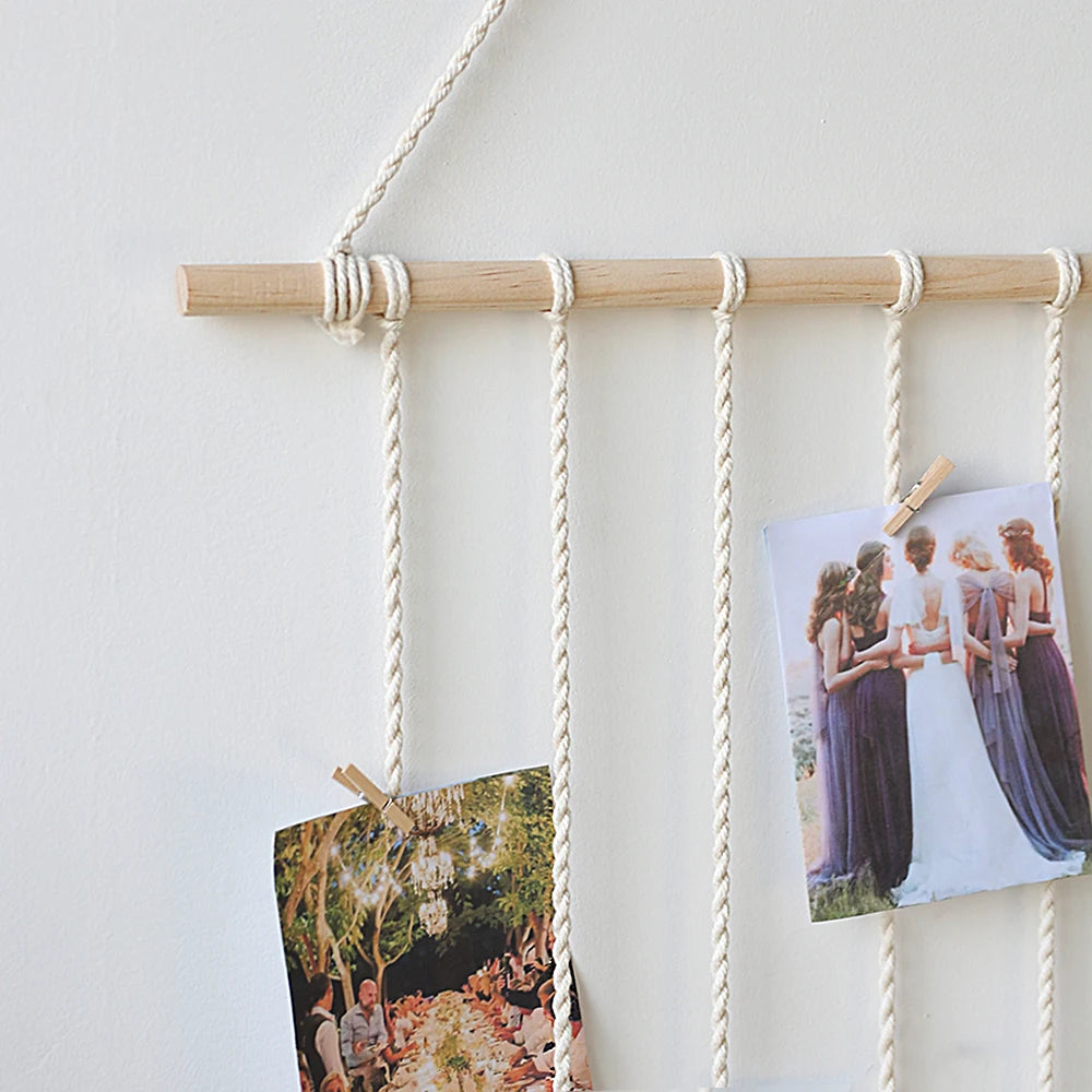 A macrame photo display featuring multiple photos hanging from a wooden bar on a white wall.