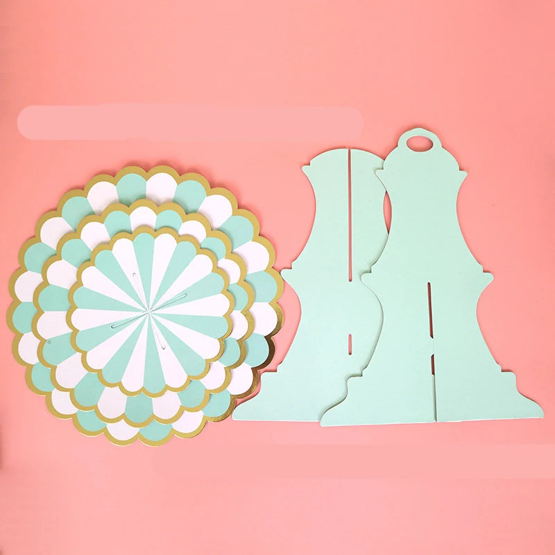 A light mint green cardboard cupcake stand with a decorative flower cutout on a pink background.