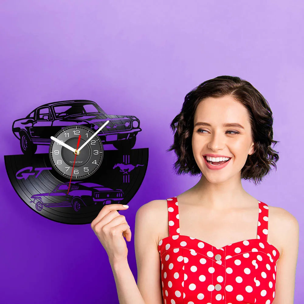 A woman holds a black vinyl record sports car wall clock against a purple background.
