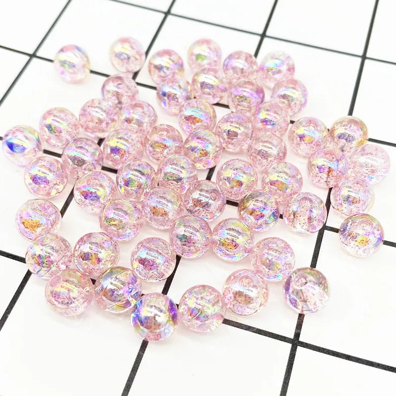 A pile of pink iridescent acrylic round beads for jewelry making scattered on a black and white grid.