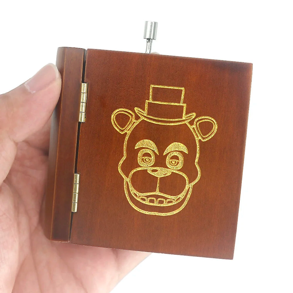 A brown wooden hand-crank music box with a carved tiger face design is held in a hand.