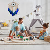 A father and child play with wooden toys in front of a handmade boho evil eye dream catcher wall decor.
