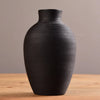 A matte black ceramic vase with vertical ribbing sitting on a wooden surface.