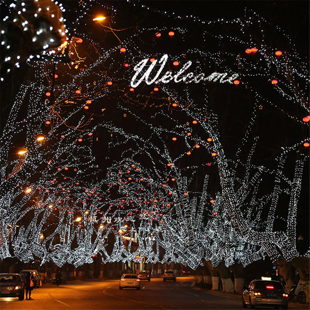 A nighttime view of a tree-lined street decorated with bright white and orange LED string lights for holiday display