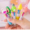 A hand holds a set of five colorful silicone cartoon-designed pen heads featuring animals like a bird, a frog, and a pink bir
