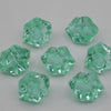 Several faceted, light green acrylic crystals of various sizes are scattered on a white surface.