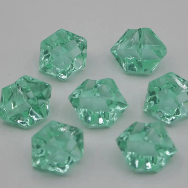 Several faceted, light green acrylic crystals of various sizes are scattered on a white surface.