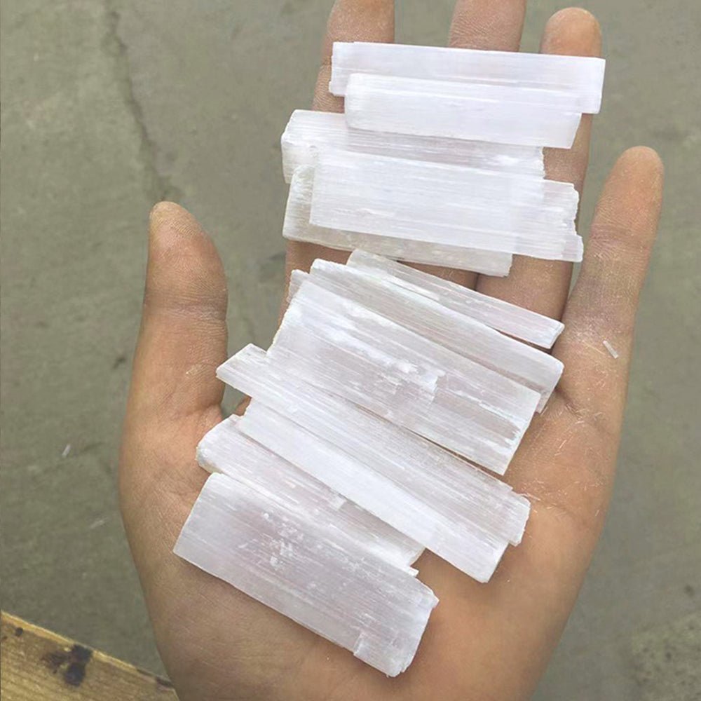 Several translucent white selenite crystal wands are held in a person's hand.