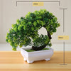 Artificial bonsai tree in a white pot with green foliage, displayed on a wooden surface.