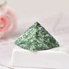 Cristal piramidal de fluorita verde natural sobre una superficie blanca con una rosa rosa desenfocada al fondo.
