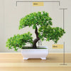 Artificial bonsai tree in a white rectangular pot with green foliage, displayed on a wooden surface.