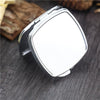 A silver mini double-sided folding makeup mirror is shown resting on a dark wooden surface.