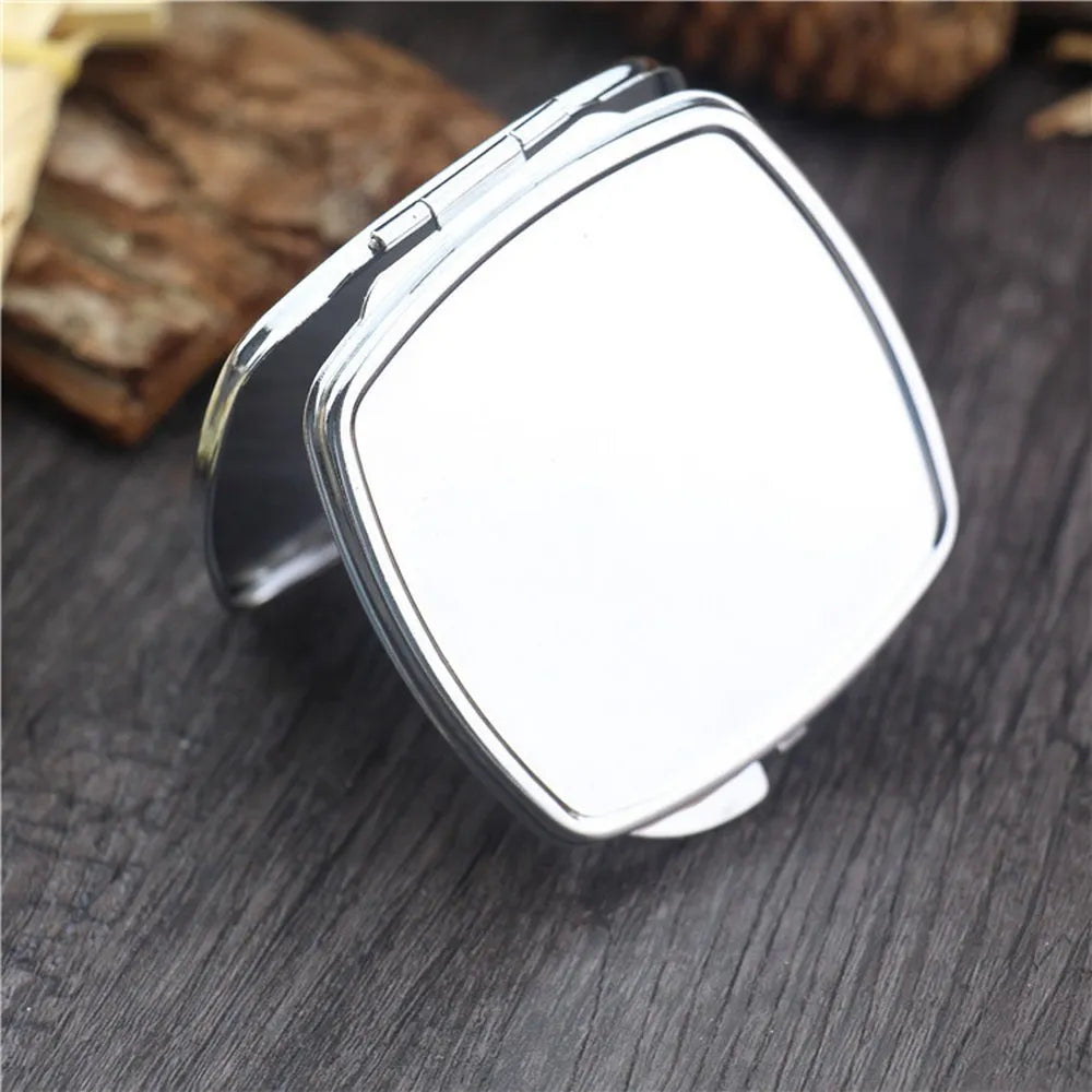A silver mini double-sided folding makeup mirror is shown resting on a dark wooden surface.
