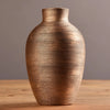 A textured, ribbed, earth-toned ceramic vase with a rounded body sits on a wooden surface.