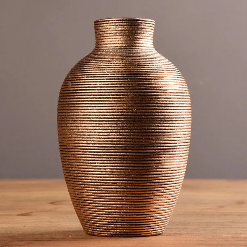 A textured, ribbed, earth-toned ceramic vase with a rounded body sits on a wooden surface.
