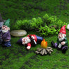 Three miniature resin gnome statues with white beards and colorful hats lying on green mossy ground.