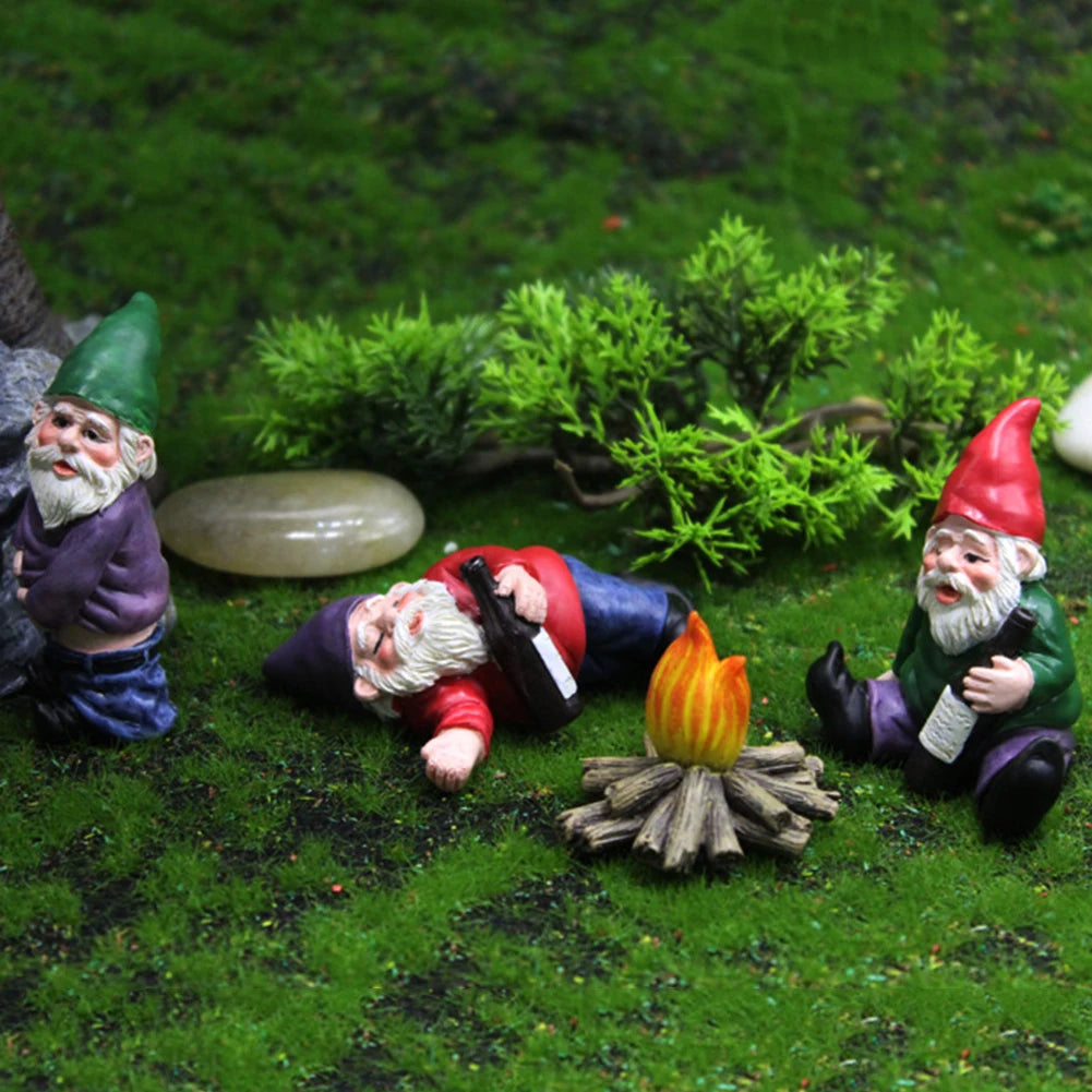 Three miniature resin gnome statues with white beards and colorful hats lying on green mossy ground.