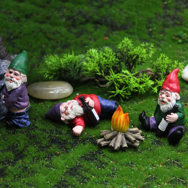 Tres estatuas gnomo de resina en miniatura con barbas blancas y sombreros coloridos, tumbadas sobre musgo verde.