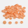 A pile of assorted light orange snap buttons, measuring 12mm and 10.5mm, for crafting.