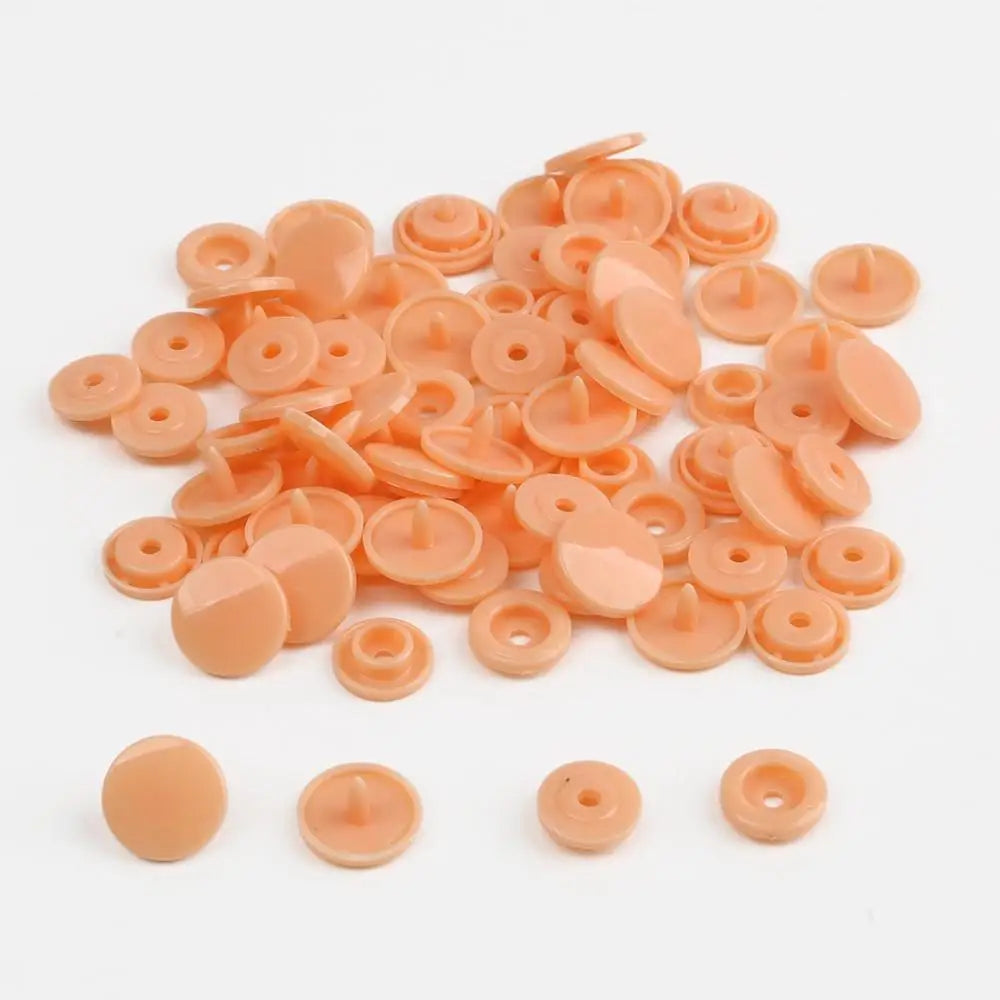 A pile of assorted light orange snap buttons, measuring 12mm and 10.5mm, for crafting.