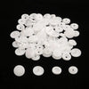 A pile of assorted white snap buttons, measuring 12mm and 10.5mm, scattered on a black surface.