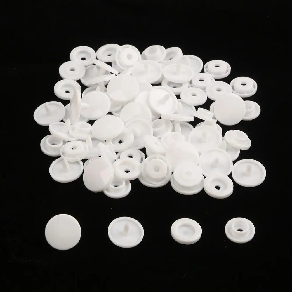 A pile of assorted white snap buttons, measuring 12mm and 10.5mm, scattered on a black surface.