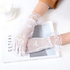 Pair of sheer white lace gloves worn on a hand, displayed next to a white cup and a book.