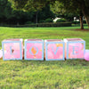 A display of clear boxes filled with pink balloons spelling out LOVE for first birthday or baby shower decorations.