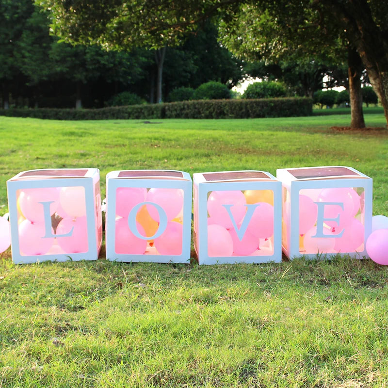 A display of clear boxes filled with pink balloons spelling out LOVE for first birthday or baby shower decorations.