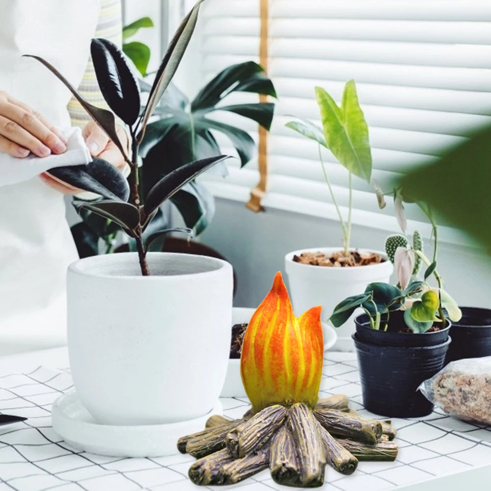 A hand is pouring white liquid onto a small plant in a white pot, with miniature resin gnome statues and wood pieces nearby.
