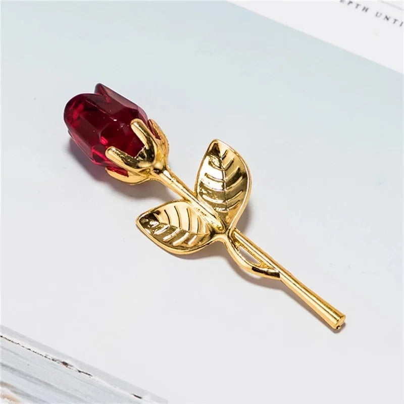 A gold-toned crystal rose artificial flower with a deep red bloom and leaves.