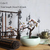 Artificial silk cherry blossom branches in a light green ceramic pot on a wooden surface.