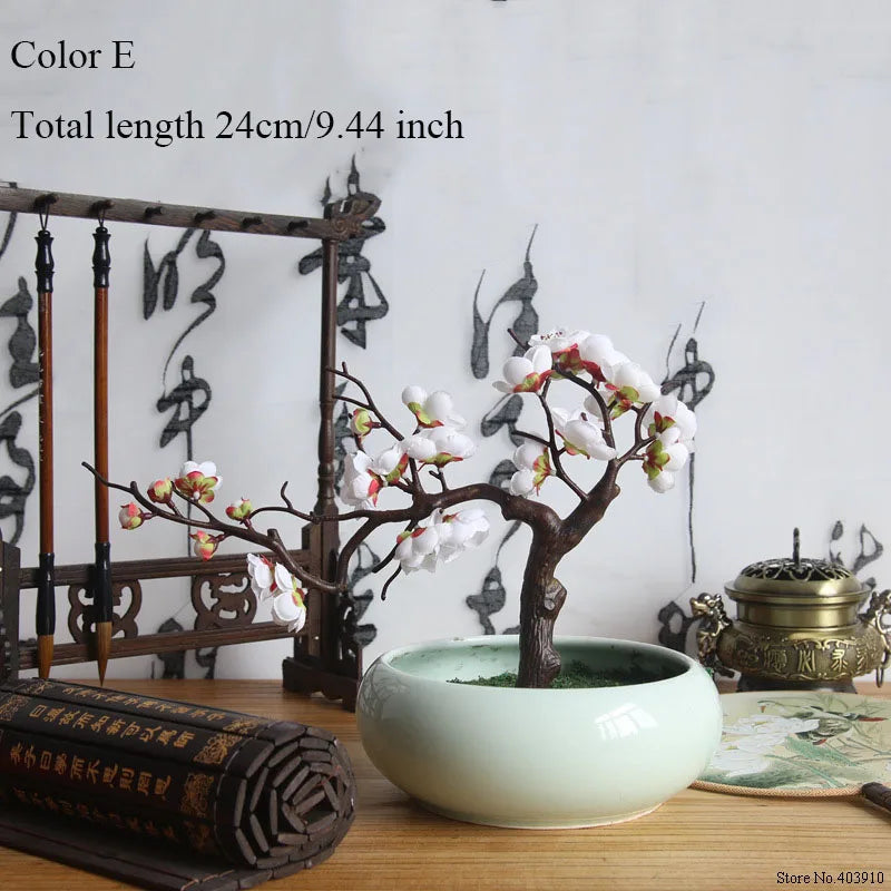 Artificial silk cherry blossom branches in a light green ceramic pot on a wooden surface.