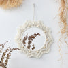 Boho macrame round wall mirror with a textured frame and natural wood accents hanging on a white wall.