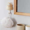 A light beige cartoon cat wall hook with a white fabric pom-pom hanging next to a wooden framed mirror.