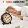 A vintage metal battery alarm clock is placed on a white surface next to a sleeping woman.