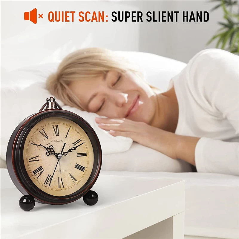 A vintage metal battery alarm clock is placed on a white surface next to a sleeping woman.