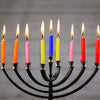 A black candelabra holds ten lit mini taper candles in various colors including orange, pink, yellow, and blue.
