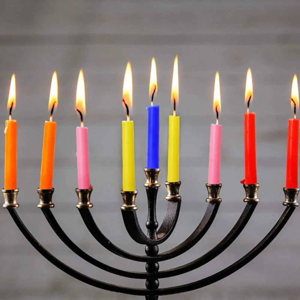 A black candelabra holds ten lit mini taper candles in various colors including orange, pink, yellow, and blue.