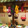 A display of lifelike artificial fruits and vegetables, including yellow and purple gourds, hanging from a wooden structure.