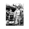 Black and white photo of a racing driver in a white suit posing next to a race car.
