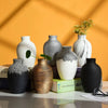 A collection of modern ceramic vases in various shades of gray, white, and black on a light surface.