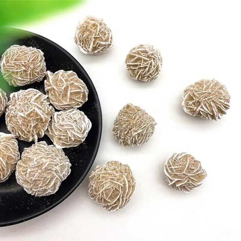 Small, round, natural desert rose selenite stones scattered on a black plate.