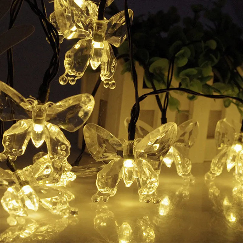 A close-up of glowing solar decorative string lights shaped like butterflies illuminating a dark background.