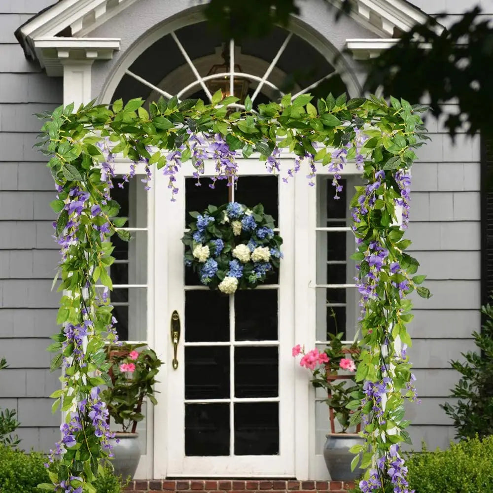 A white door framed by a lush green wisteria garland and a blue floral wreath.