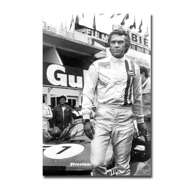 A black and white photo of a man in racing attire standing next to a race car.
