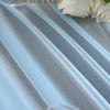 Light blue sheer chiffon fabric draped in vertical pleats with white roses and a glass object.